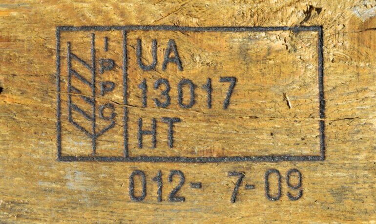 A close-up view of a wooden pallet's fire-branded ISPM label including a series of letters and numbers.