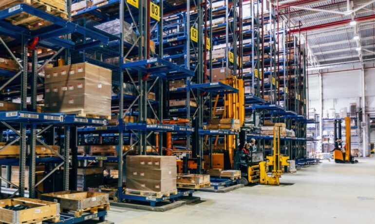 The interior of a modern warehouse shows floor-to-ceiling shelving, forklifts, workers, and stored items.