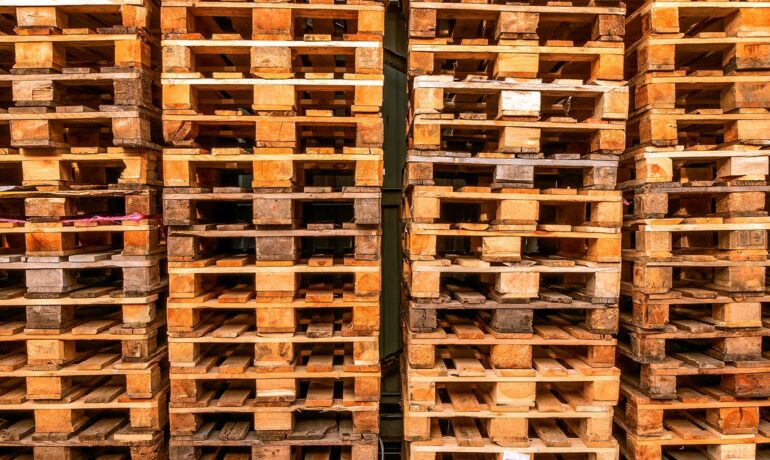 Stacks of wooden pallets in tall rows, showing weathered surfaces and uniform structure in a storage setting.
