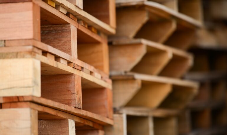 A close-up of stacked wooden pallets with repeating slats highlights the texture and structure in the wood.