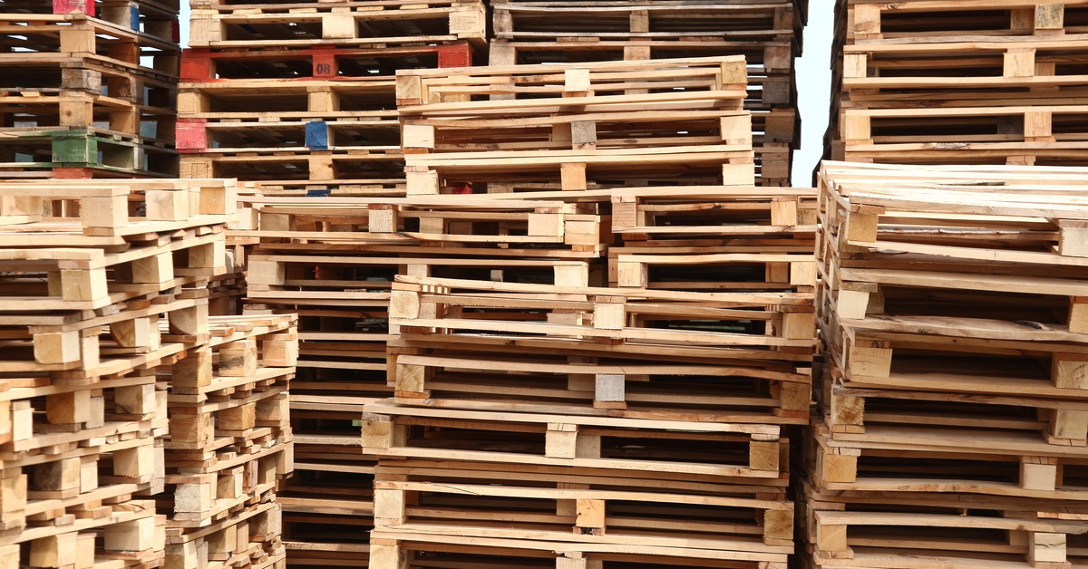 Stacks of wooden shipping pallets are piled in an outdoor storage yard with varying heights and weathered textures.