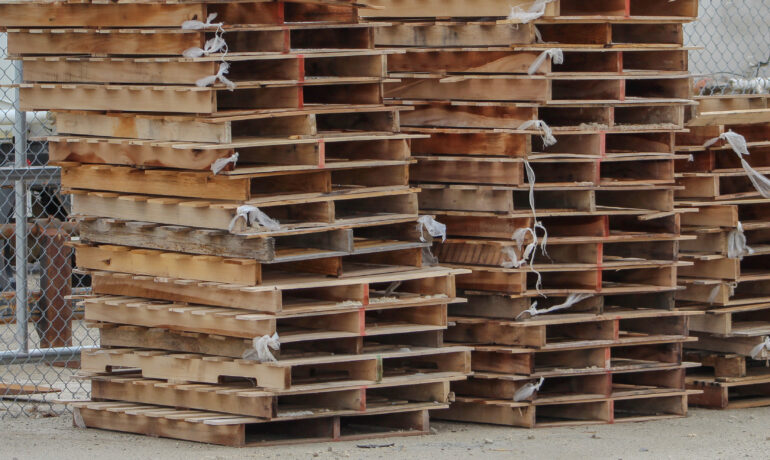 Stacks of used wooden pallets are piled outdoors in an industrial storage yard, ready for shipping, recycling, or reuse.
