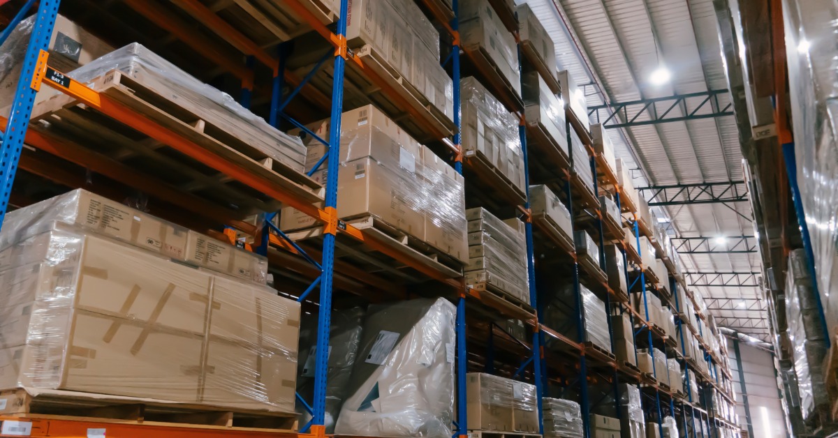 Tall warehouse shelving stocked with boxed inventory and palletized goods in a large distribution center.