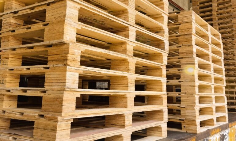 Three stacks of new wooden pallets sit along the edge of a warehouse loading area, organized for storage and transport.