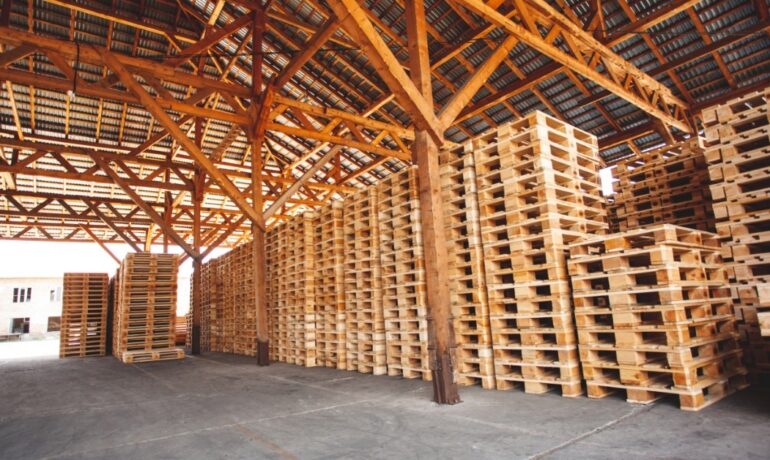 Stacks of wooden pallets fill a warehouse storage area, providing inventory to support increased shipping demand.