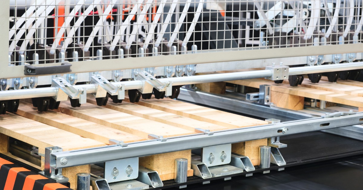 A wooden pallet moves through automated equipment that guides and positions pallets during warehouse operations.