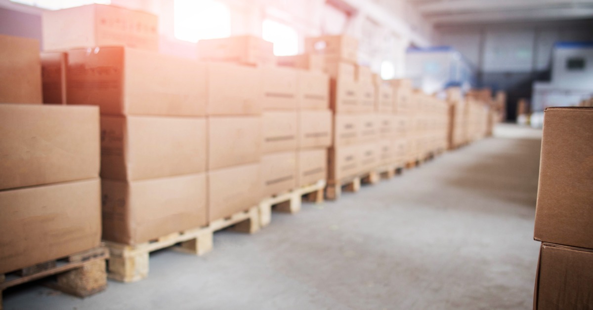 Cardboard boxes are arranged on wooden pallets in a warehouse, and the pallets are lined up in a row.