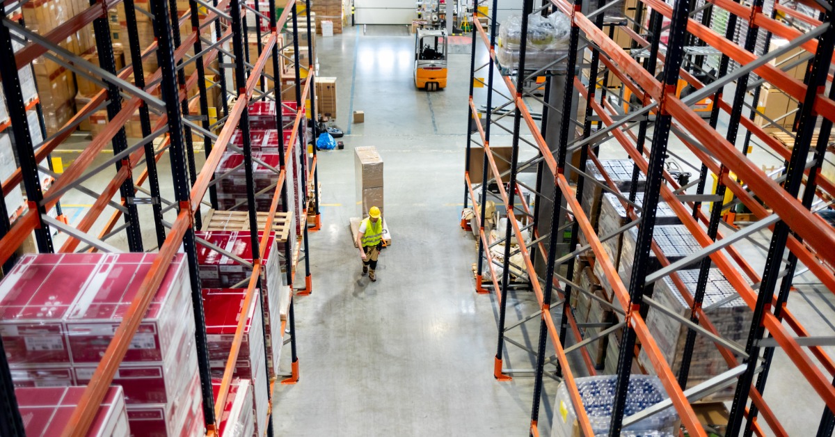 An overhead view of a warehouse aisle with palletized products stored on tall industrial racks and workers below.